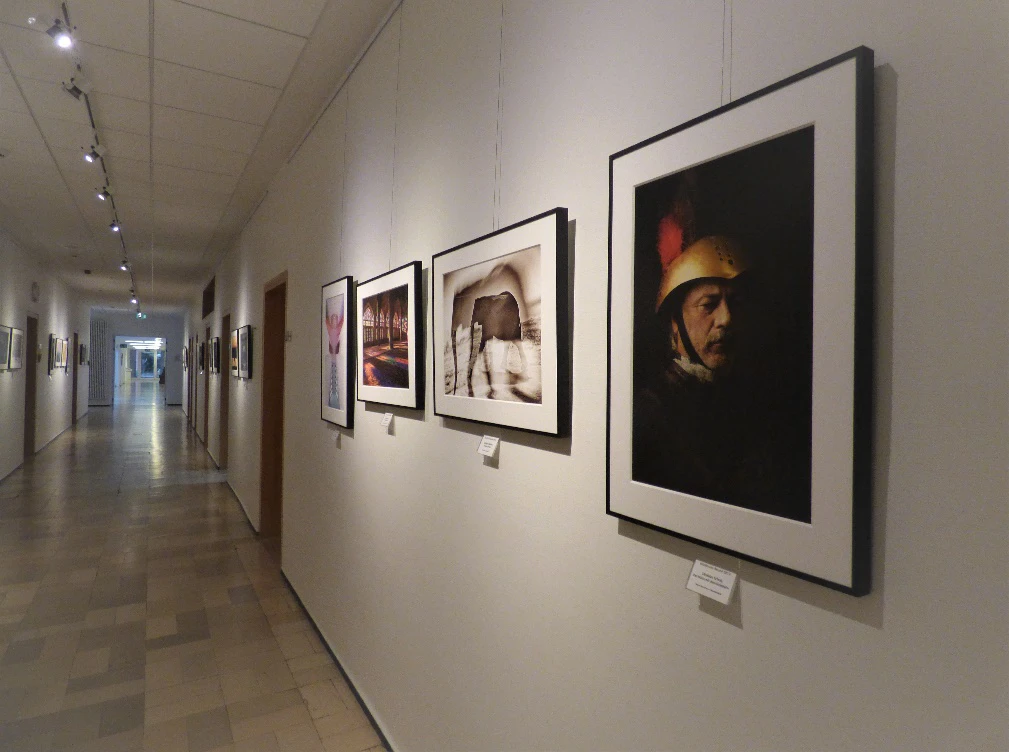 In einem Flur der Katholischen Akademie Stapelfeld hängen Bilder in verschiedenen Größen in unterschiedlichen Rahmen an der Wand.