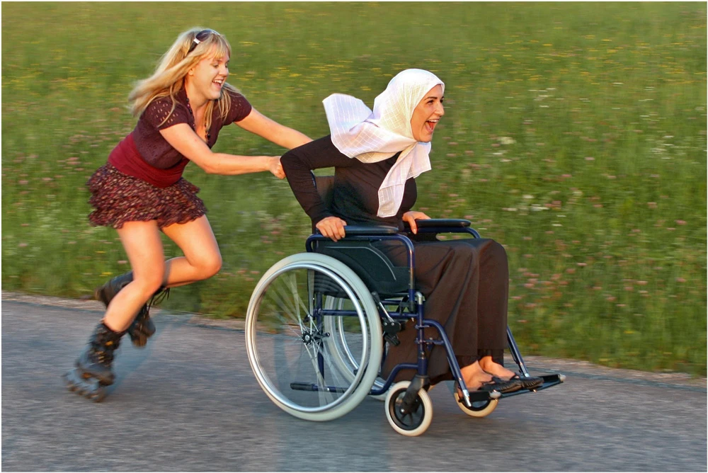 Eine Person auf Inlinern schiebt eine Person im Rollstuhl.