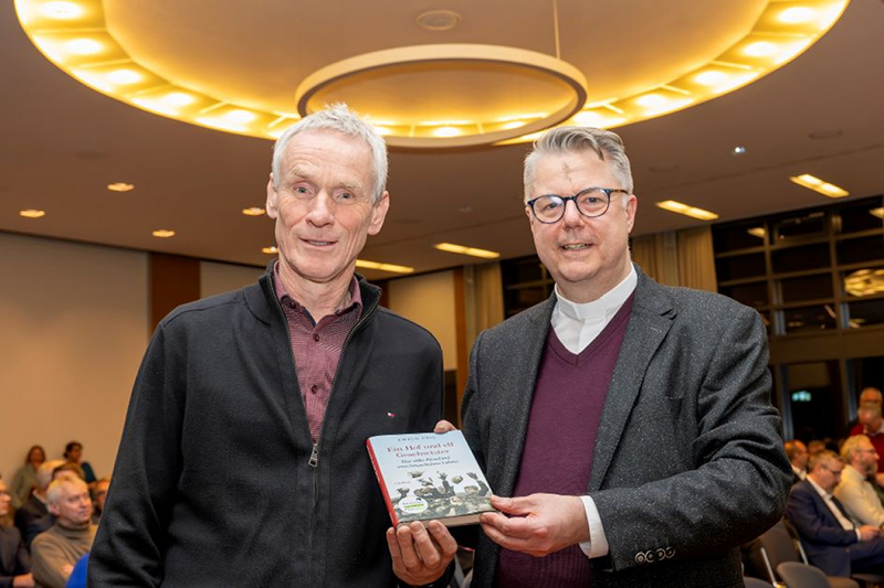 Prof. Dr. Frie und Pfarrer PD Dr. Marc Röbel präsentieren ein Buch in die Kamera.