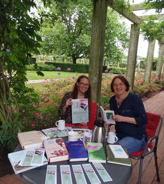 Marianne Hettrich und Kerstin Graumann sitzen mit einem Stapel Bücher im Garten