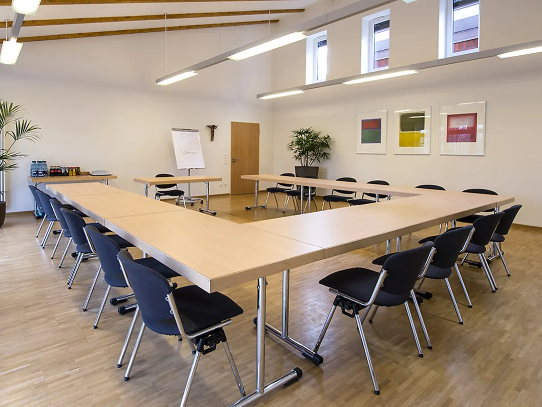 In einem großen Seminarraum mit Parkettboden stehen acht Tische in einem U angeordnet und mit Stühlen versehen.